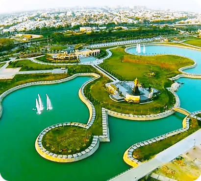 Aerial view of a large, green park with a water body and buildings in Lucknow. Keywords: Lucknow park, aerial view, urban green space, scenic.